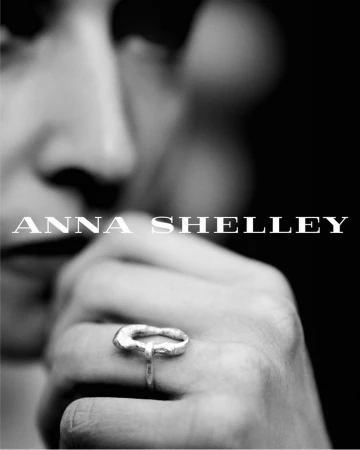 Close-up in black and white of a hand wearing an organic sculptural silver ring with a softly blurred face in the background.
