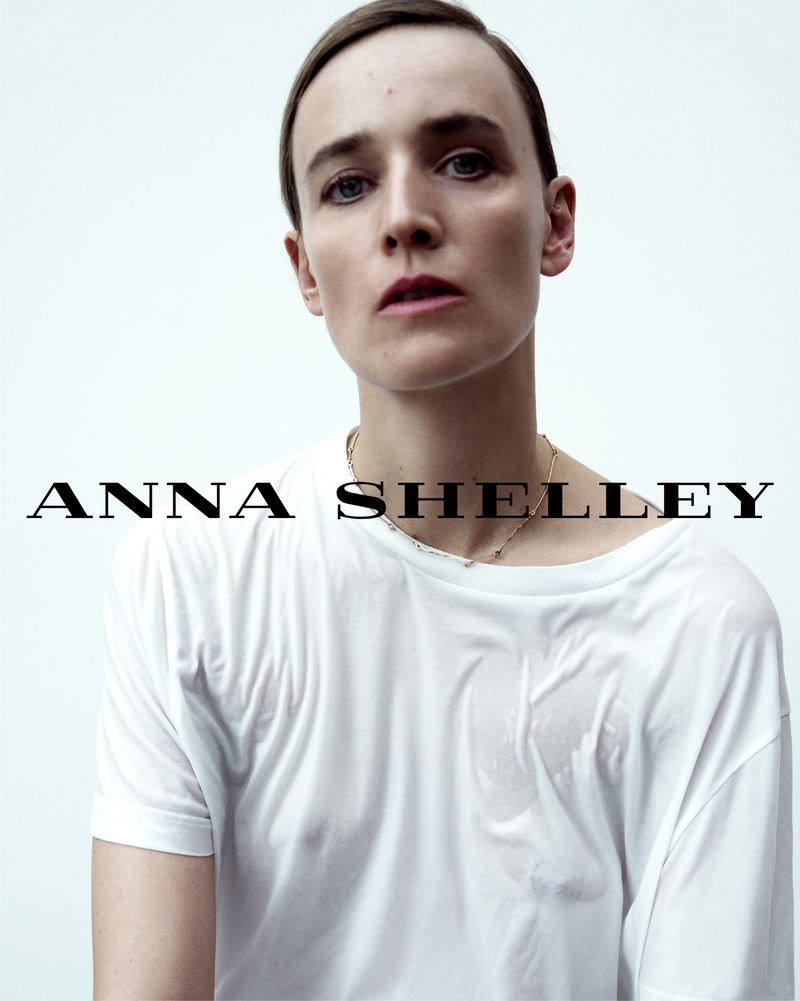 Model Anne-Catherine Lacroix wearing a thin white t-shirt and gold chain necklace against a white background.