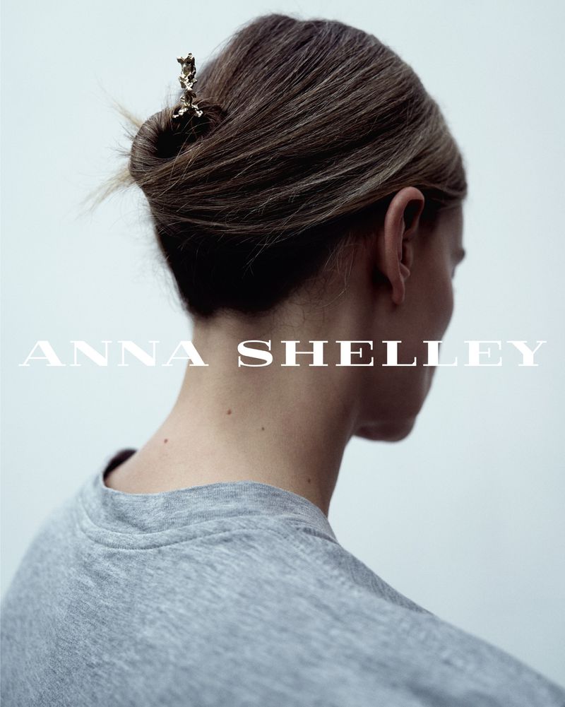 Close-up studio shot of woman's hair styled in a bun with a decorative gold hair clip. She wears a gray shirt in the bright, diffused light.