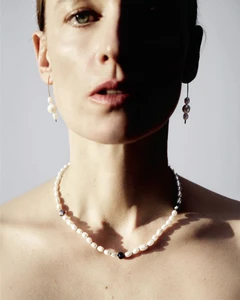 Model Anne-Catherine Lacroix wearing a white pearl necklace and matching drop earrings against a neutral studio backdrop.