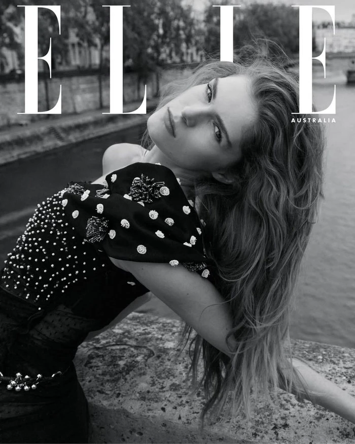 Monochrome fashion editorial portrait of a woman in a heavily embellished black dress leaning outdoors by water