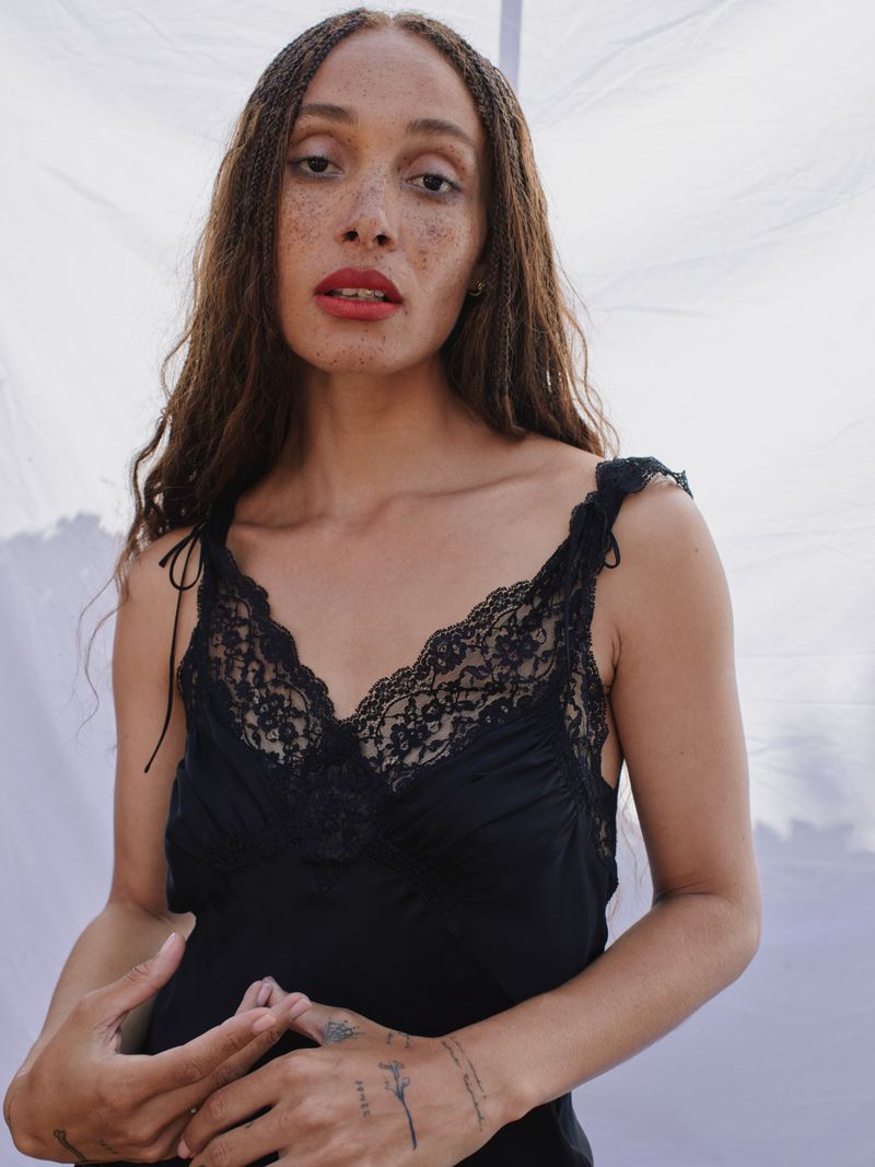 Elegant portrait of a woman with freckles in a black lace-trimmed slip dress against a bright white background. Fashion and beauty concept.