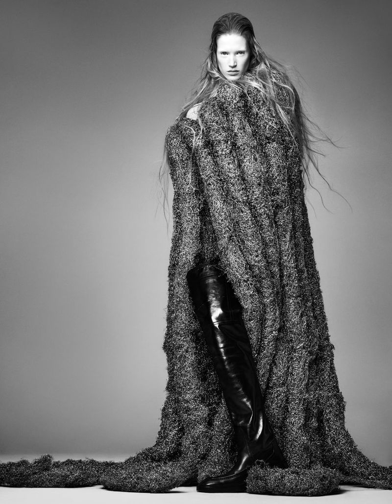 Black and white fashion portrait: a model poses draped in a woven garment with an over-the-knee leather boot.