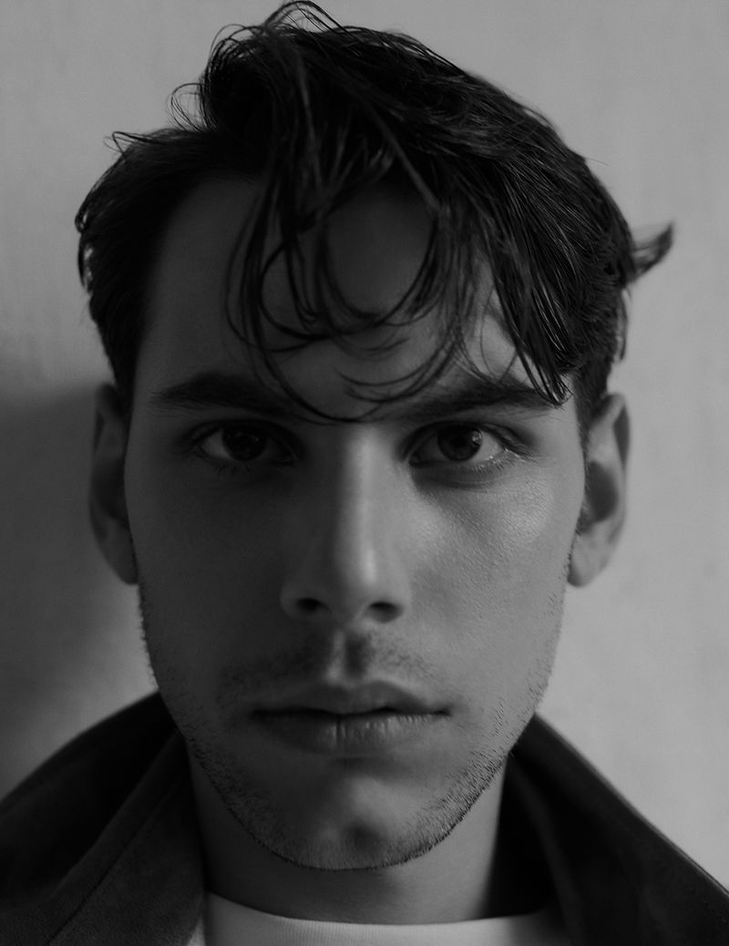 Monochromatic portrait of a young adult male with dark hair, facing forward with a serious expression, in front of a plain background.