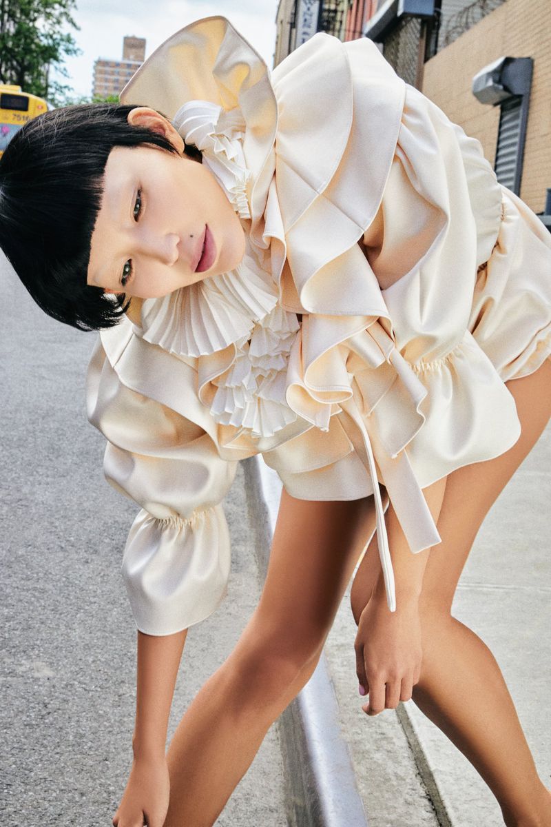 Woman poses in a ruffled, cream-colored garment on an urban street, showcasing high fashion and unique style against the city backdrop.