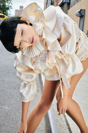 Woman poses in a ruffled, cream-colored garment on an urban street, showcasing high fashion and unique style against the city backdrop.