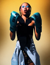 Model wearing teal boxing gloves and a black top against a warm gold backdrop for Cosmopolitan Slovenia