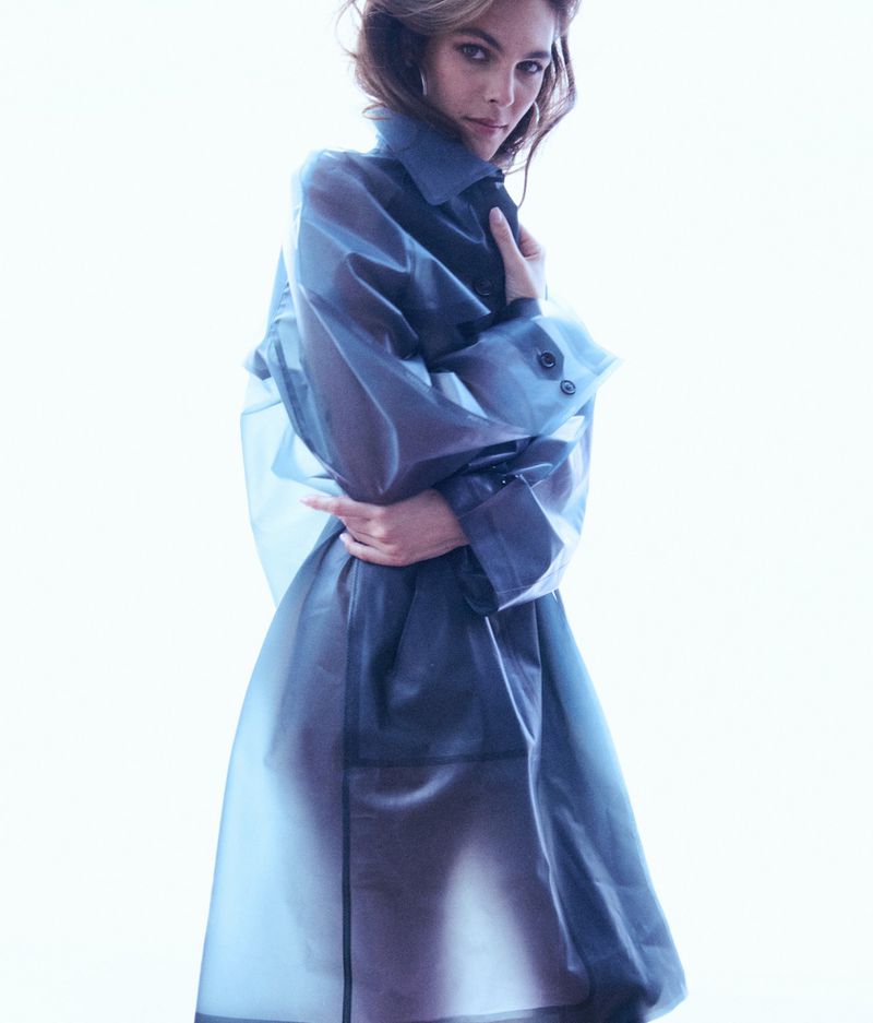 Portrait of a woman in a translucent blue trench coat against a white background, showcasing a modern fashion style and elegant studio lighting.