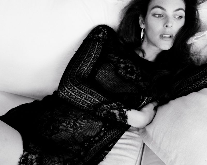 Monochrome portrait of a young woman in a black lace dress lying on a white surface, showcasing a blend of beauty and fashion.