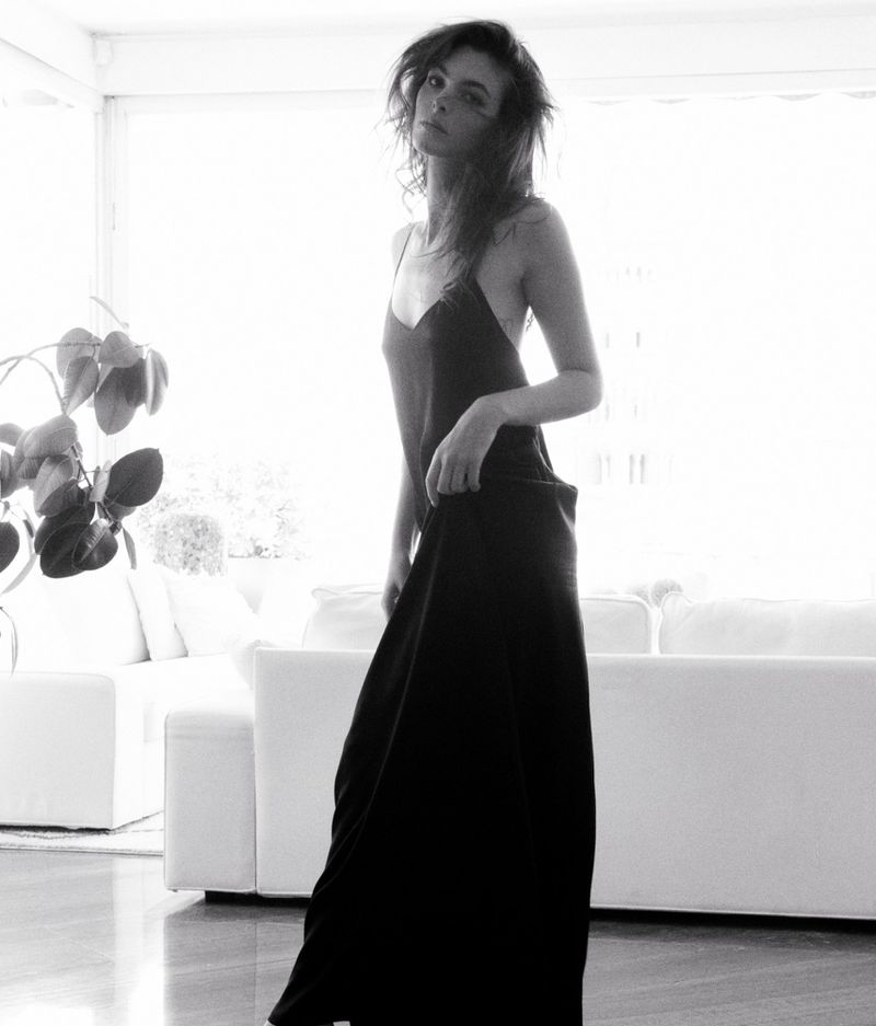 Model Vittoria Ceretti in a black slip dress standing in a light-filled living room for D Repubblica