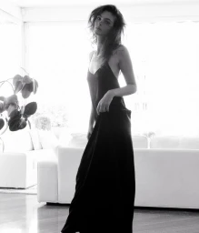Model Vittoria Ceretti in a black slip dress standing in a light-filled living room for D Repubblica