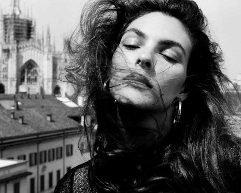 Close-up monochrome portrait of model Vittoria Ceretti with wind-blown hair against a city rooftop background.