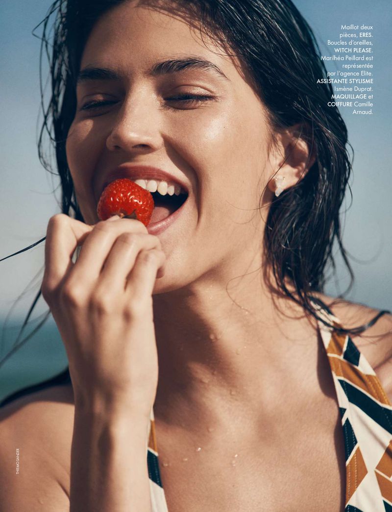 Close-up of a wet-haired woman eating a strawberry on the beach, wearing a patterned bikini top, wet hair, eyes closed in delight.