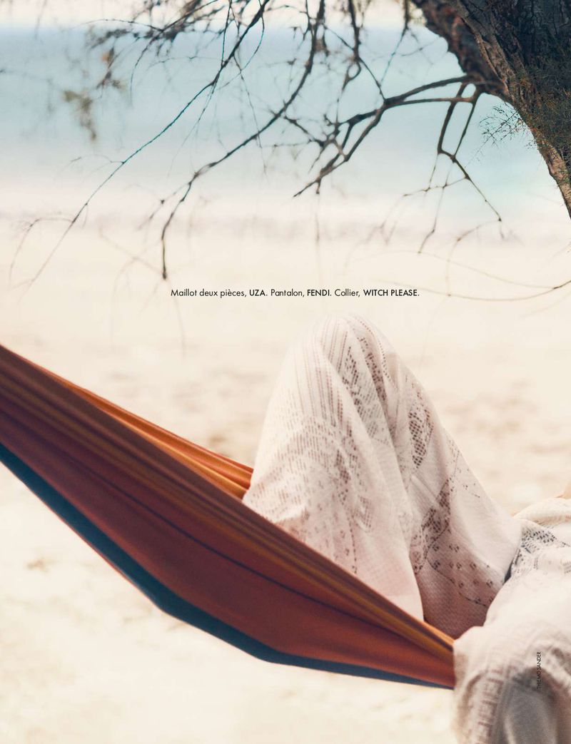 Woman in hammock relaxing at beach. She is covered with white lace garment, tree and ocean visible, creating serene lifestyle image.