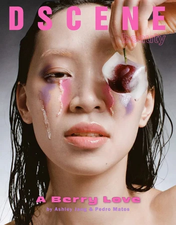 Magazine cover featuring a woman with creative pink and purple makeup, holding a cherry with ice on her eye in a close-up shot.