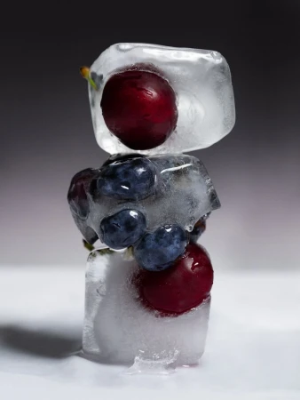 Stacked ice cubes with frozen blueberries and cherries creating a refreshing food still life against a grey gradient backdrop.
