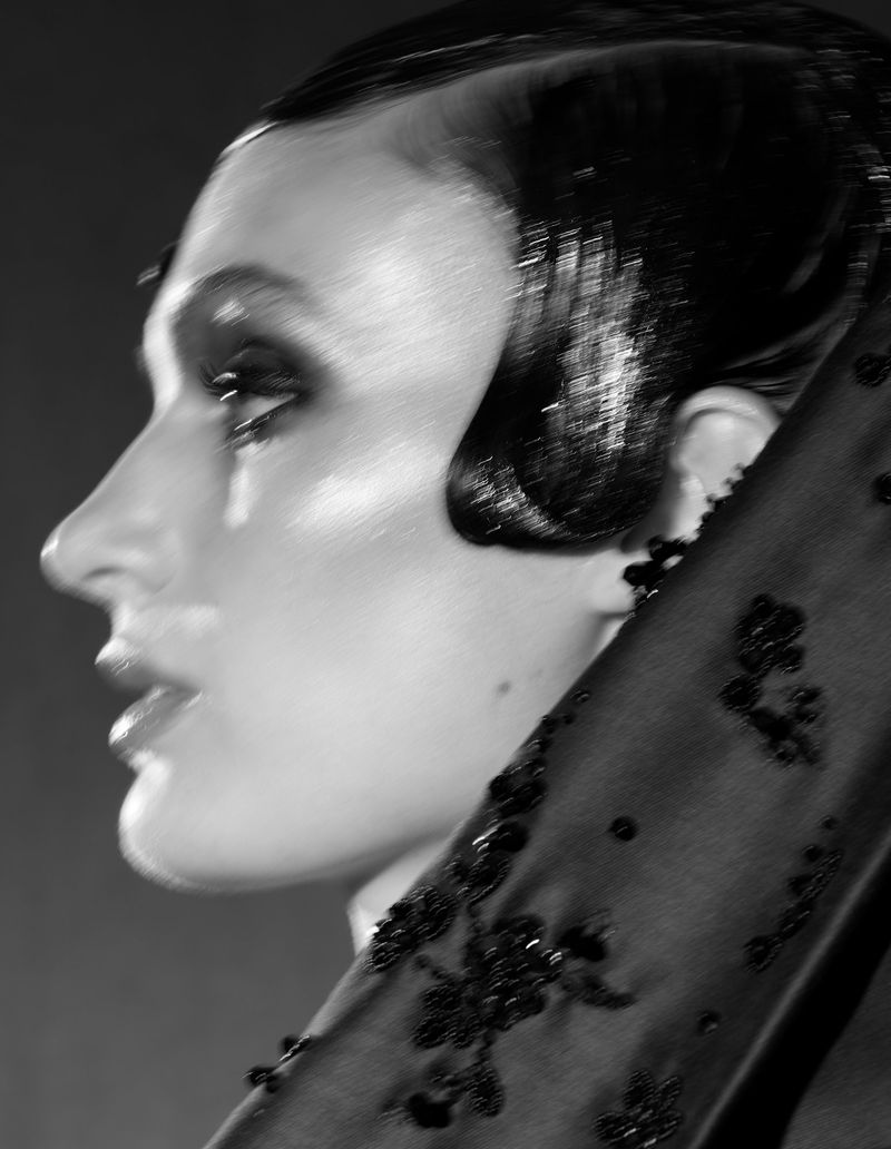 Monochrome portrait of an adult woman in profile, wearing beaded head covering and dark eye makeup, showcasing a vintage hairstyle.