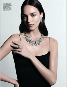 Model wearing diamond and emerald necklace and earrings with a black top against white background
