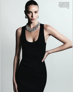 Model wearing a black tank dress and sparkling statement necklace against a light grey background