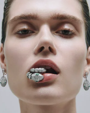 Close-up portrait of a model holding a jeweled snake ring in her mouth, wearing matching drop earrings for L'Officiel Malaysia.