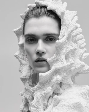 Close-up portrait of a model wearing a sculptural white textured headpiece against a neutral background