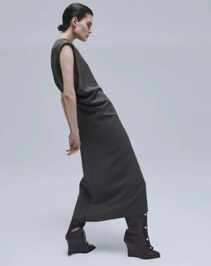 Model wearing a dark sleeveless dress and tall wedge boots against a plain grey studio backdrop
