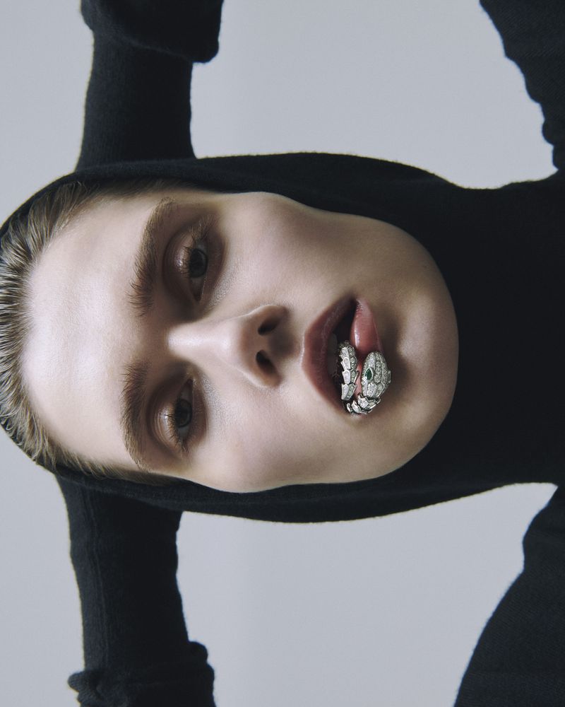 Model wearing a black hooded top with a jeweled snake ring in her mouth against a grey studio backdrop
