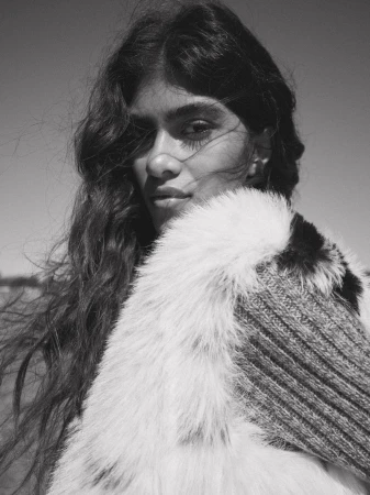 Black and white portrait of an adult woman with long hair, wearing a fur collar and knit garment against a clear sky.