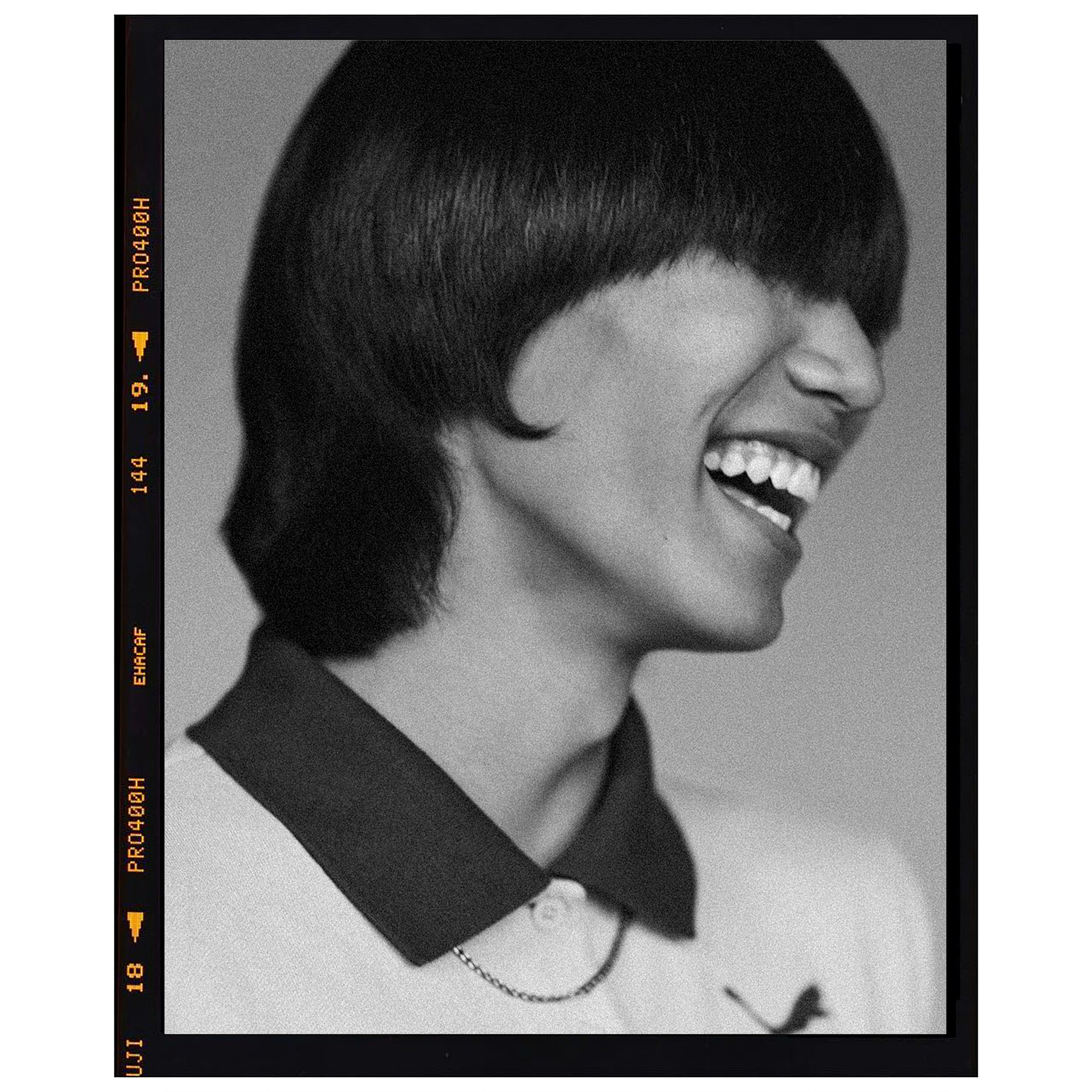Monochrome portrait of an adult smiling with short, dark hair, wearing a collared shirt, captured in a film-like aesthetic with border details.