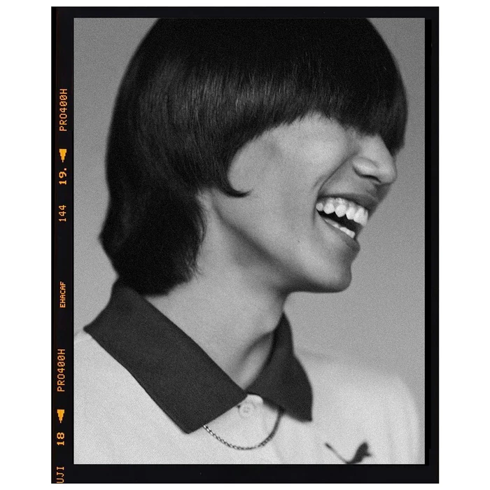 Monochrome portrait of a laughing person with dark bangs and a collared polo shirt, framed with film borders.