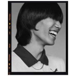 Monochrome portrait of a laughing person with dark bangs and a collared polo shirt, framed with film borders.