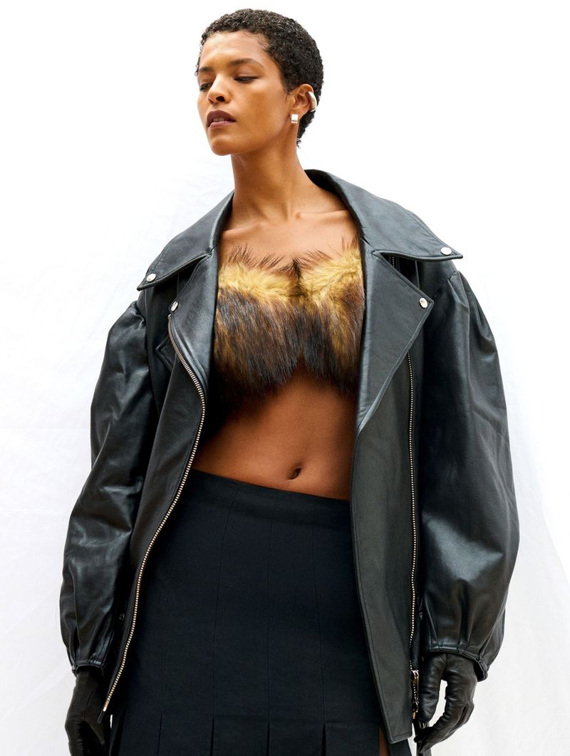Fashion portrait of a woman wearing a black leather jacket and black skirt against a white backdrop, showcasing contemporary style.