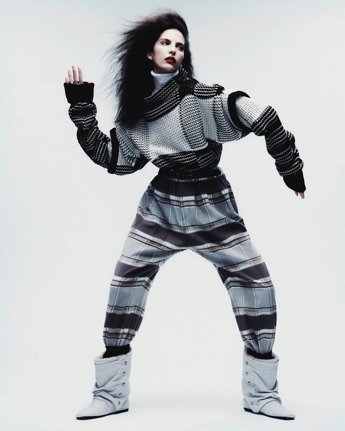 Model Africa Garcia in patterned knitwear and plaid trousers with windblown hair against a white background for Vogue Mexico