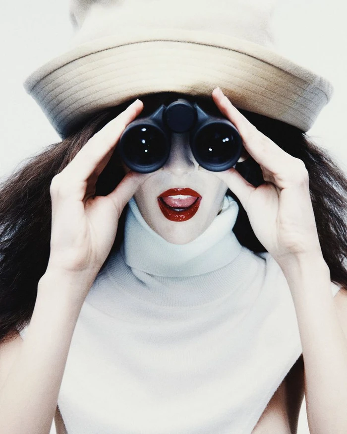 Model Africa Garcia holding binoculars to her eyes wearing a wide-brimmed hat and white turtleneck for Vogue Mexico