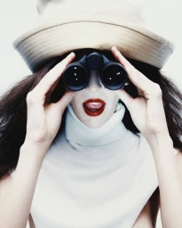 Model Africa Garcia holding binoculars to her eyes wearing a wide-brimmed hat and white turtleneck for Vogue Mexico