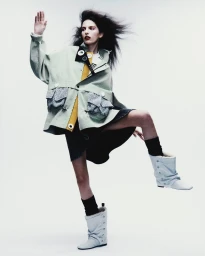 Model Africa Garcia in a sage green jacket and white boots posing against a white studio background for Vogue Mexico
