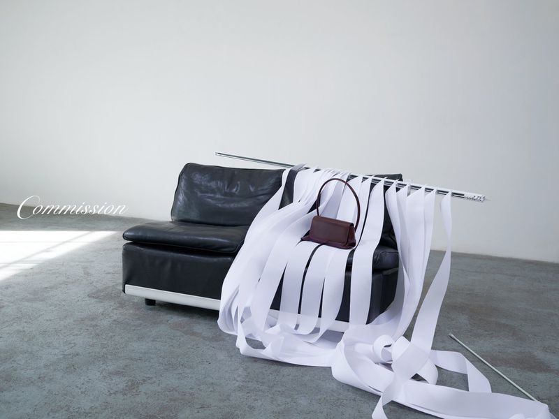 Elegant brown leather handbag showcased on a black leather sofa, adorned with flowing white ribbons in a minimalist studio setting.