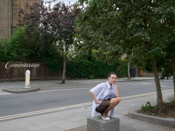 Woman squatting on a concrete block on a city street wearing an oversized striped shirt, dark skirt, and white heels.