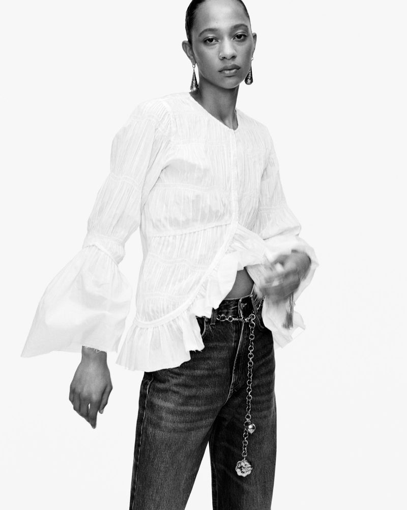 Monochrome portrait of an adult woman wearing a ruffled top and jeans, posing in a photo studio against a bright white backdrop.
