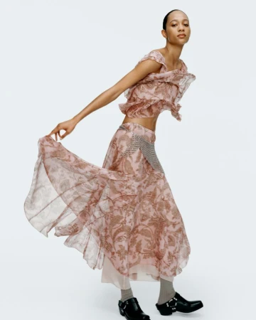Selena Forrest poses in a ruffled patterned crop top and matching flowing skirt against a white studio background.