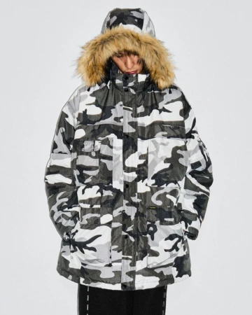 Person wearing a hooded camo puffer jacket with fur trim in a studio setting, showcasing winter fashion and outerwear.