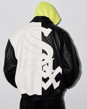 Person wearing a black and white Chicago White Sox leather bomber jacket with a yellow hoodie on a neutral background in a studio setting.