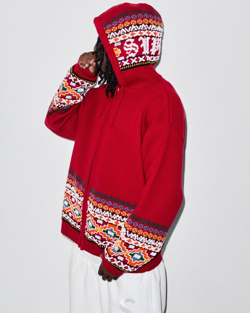 Person in red, patterned hooded sweater and sweatpants stands against a light background. The sweater is patterned on the sleeves and hood.