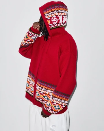 Person in red, patterned hooded sweater and sweatpants stands against a light background. The sweater is patterned on the sleeves and hood.