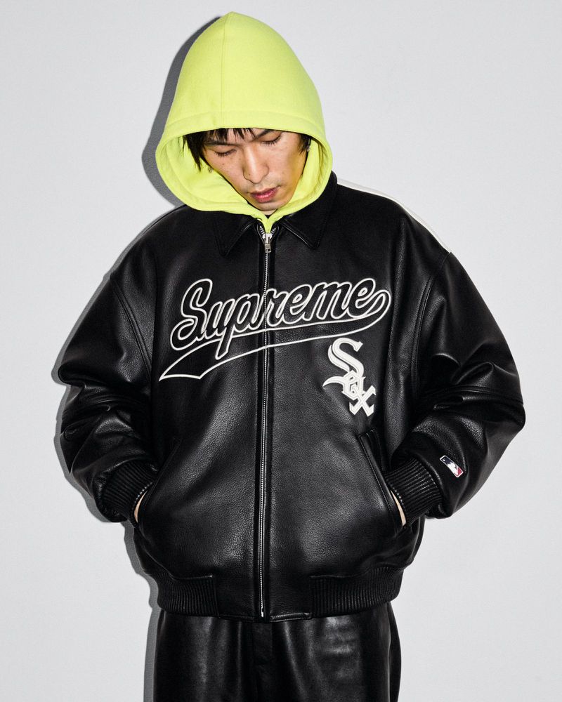 Adult male wearing black leather jacket with 'Supreme' logo and neon yellow hoodie, in a studio setting with neutral background.