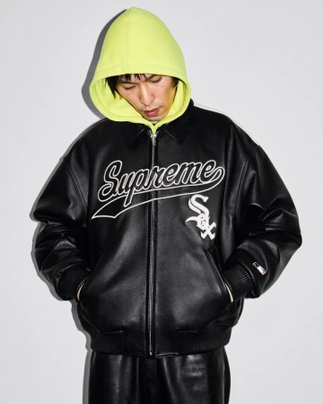 Adult male wearing black leather jacket with 'Supreme' logo and neon yellow hoodie, in a studio setting with neutral background.