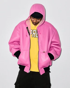Model wearing a pink hooded leather jacket over a yellow shirt and black cargo pants against a white background.