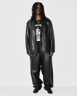 Model with long dreadlocks wearing a black leather jacket and matching pants against a plain white background for Supreme.