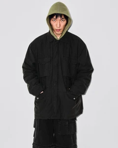 East Asian male model wearing an olive green hood under an oversized black utility jacket against a neutral studio backdrop.