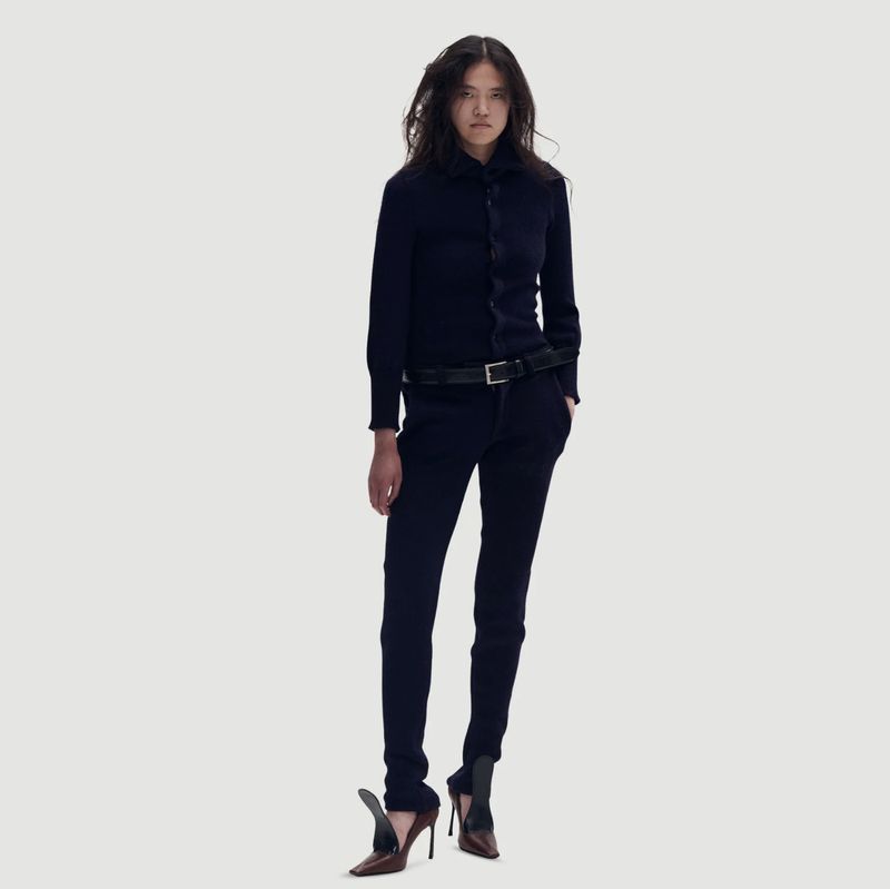 Full-length shot of a young adult female model in a navy-blue zip-up jacket and trousers, posing against a bright white studio backdrop.